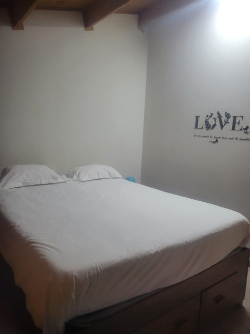 Quarto aconchegante em Casa do Criado Gerês com roupa de cama branca, vigas de madeira e decoração 'LOVE' na parede