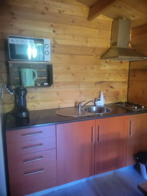 Cozinha moderna em Cabanas do Amor, Gerês com paredes de madeira, bancada escura, armários vermelhos, micro-ondas e fogão a gás