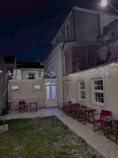 Albergue Santiago de Caminha courtyard at night with wooden chairs and tables on stone patio, Caminha Portugal hostel