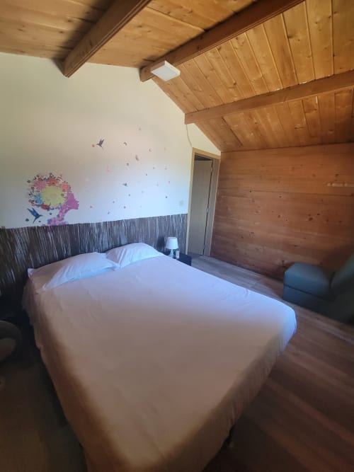 Quarto aconchegante de madeira na Casa do Criado Gerês com cama branca, decorações na parede e teto de madeira aparente