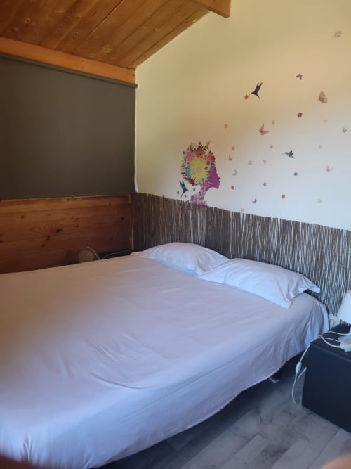 Quarto aconchegante na Casa do Criado Gerês com roupa de cama branca, vigas de madeira e adesivos coloridos de borboletas em Gerês.