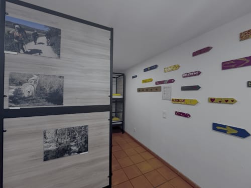 Hostel corridor with black and white photos on left wall and colorful wooden signs on right at Albergue Santiago de Caminha