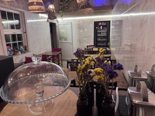 Hostel common area with purple and yellow dried flowers, glass cake dome, and dining setup at Albergue Santiago de Caminha in