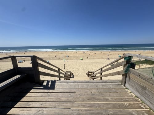 Escaliers en bois menant à la plage de sable avec océan et baigneurs à Mimizan, France