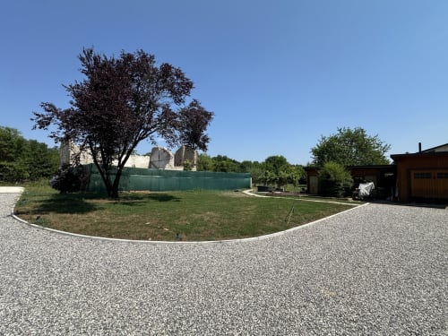 Cortile di Casale Rusignûl con vialetto ghiaioso, prato verde, albero scuro e rustici edifici in pietra a Basegliano, Italia