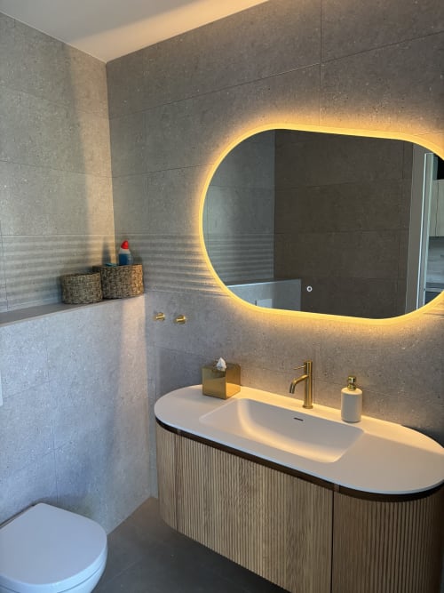 Salle de bains moderne à la Résidence Les 3 Volcans avec miroir ovale illuminé, lavabo blanc et carrelage foncé