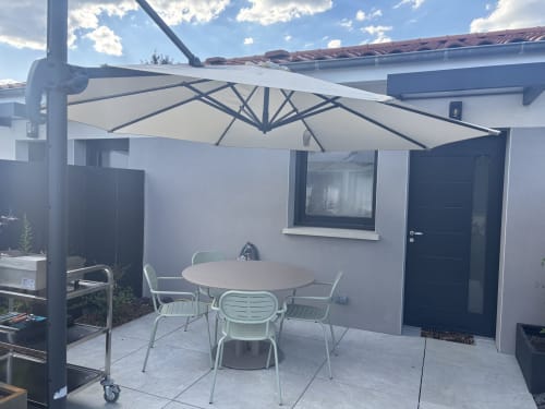 Terrasse extérieure de la Résidence Les 3 Volcans avec table ronde, chaises blanches et parasol suspendu à Clermont-Ferrand