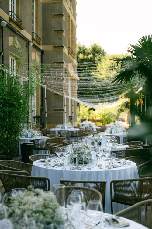 Elegant outdoor dining courtyard at Ô Château hotel in Hayange with round tables, string lights, and lush greenery
