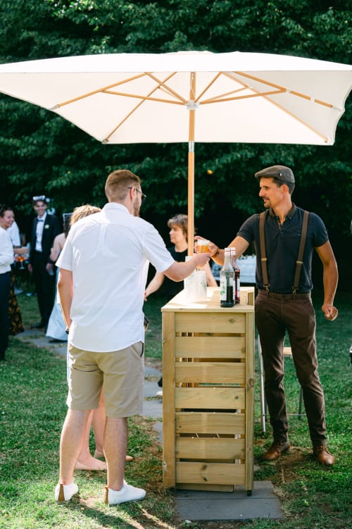 Outdoor bar service at Ô Château hotel, Hayange, with bartender serving guest under cream umbrella
