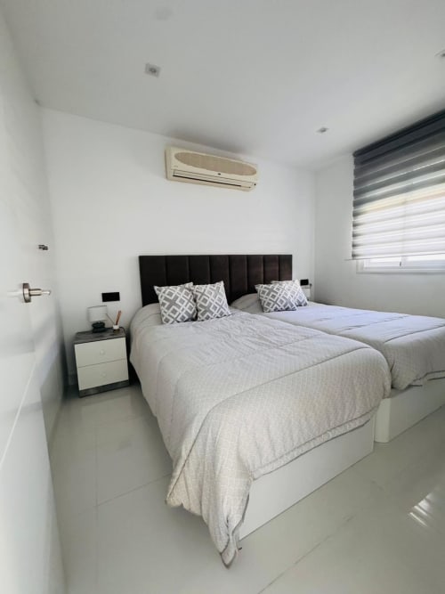 Dormitorio moderno con camas gemelas, cabecero negro, ropa de cama blanca, aire acondicionado y persianas rayadas en apartamento ALTOVELOO MAR