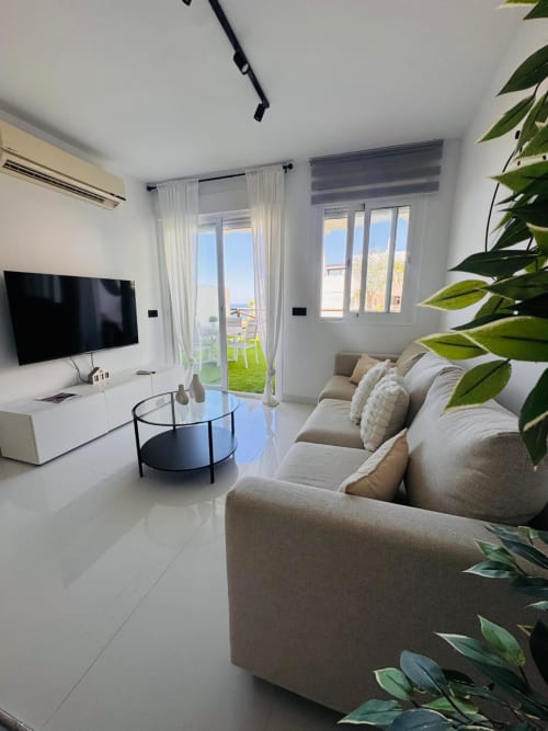 Sala de estar moderna con vista al mar, sofá beige, TV de pantalla plana, mesa de centro redonda y acceso a terraza en Torre de