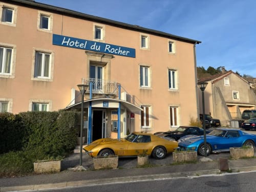 Hôtel du Rocher au Caylar, France avec sa façade pêche et voitures de sport vintage garées devant