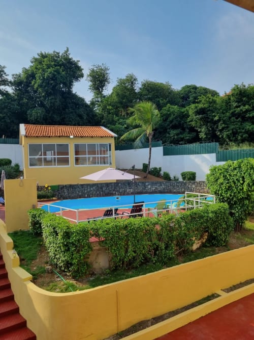 Casa amarela com quadra de ténis azul na Equador Houses em São Tomé, cercada por jardins tropicais