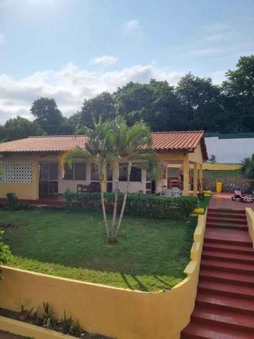 Casa Amarela - chalé em Equador Houses, São Tomé, com paredes amarelas, telhado de barro, palmeira, jardim exuberante e detalhes em vermelho