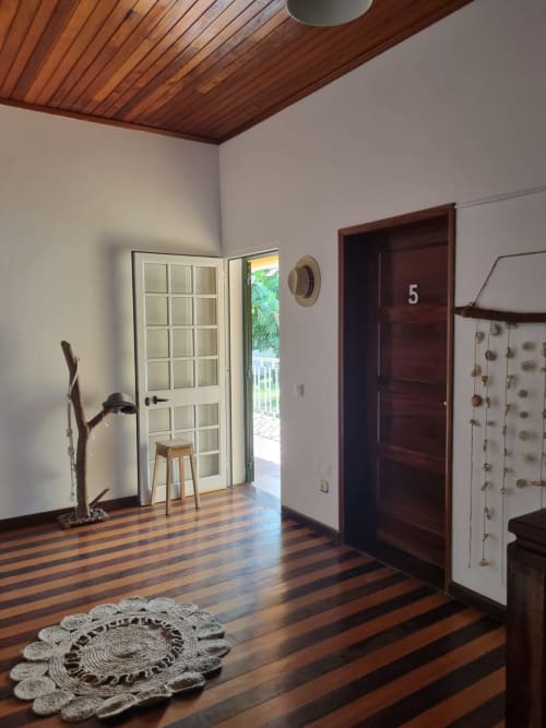 Entrada da casa de campo Casa Amarela na Equador Houses, São Tomé, com teto de madeira, portas escuras e pisos de madeira listrada.