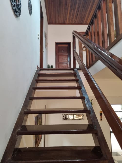 Escada de madeira com corrimãos escuros na pousada Ecuador Houses em São Tomé, levando à entrada do quarto do andar superior