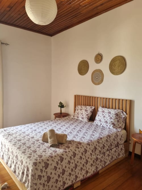 Quarto aconchegante na casa Amarela, Equador Houses em São Tomé, com cabeceira de madeira e cestos de palha na parede