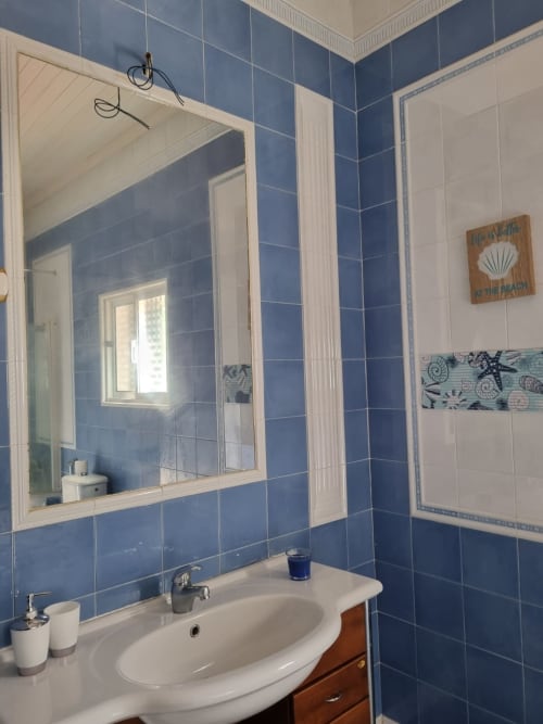 Banheiro Casa Amarela em Equador Houses, São Tomé: paredes com azulejos azuis, pia branca, espelho emoldurado, decoração com tema praia