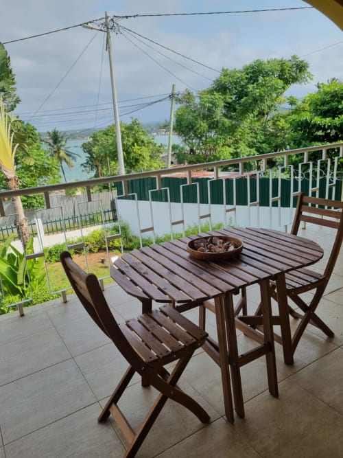 Mesa e cadeiras de madeira na varanda das Equador Houses em São Tomé, com vista para o jardim e baía