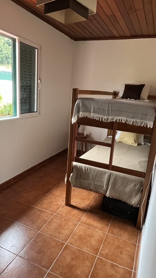 Quarto de loft aconchegante na pousada Ecuador Houses em São Tomé com cama beliche de madeira, piso de terracota e vista para o jardim