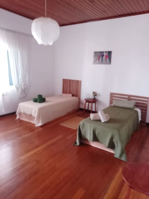 Quarto geminado luminoso na pousada Casa Amarela, Equador Houses, São Tomé, com piso de madeira vermelha e vista para o jardim