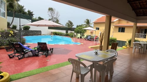 Área da piscina da Equador Houses com espreguiçadeiras, mesa de jantar e chalé amarelo em São Tomé
