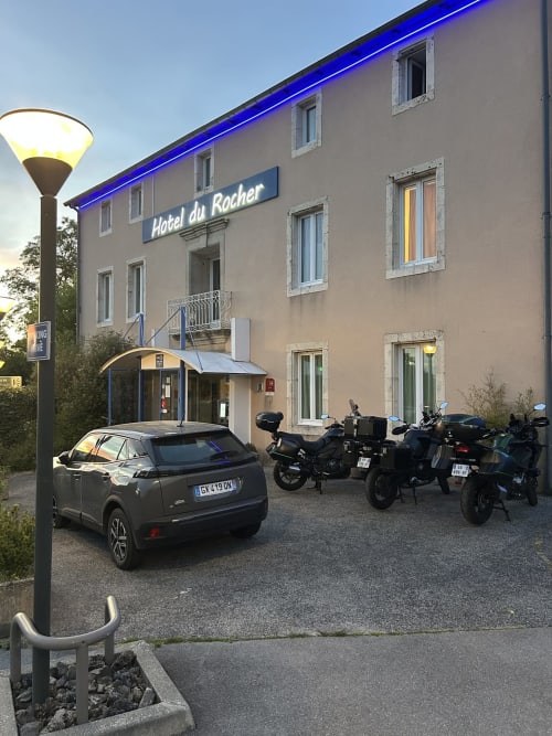 Entrée de l'Hôtel du Rocher au Caylar avec voiture garée et motos à la tombée de la nuit