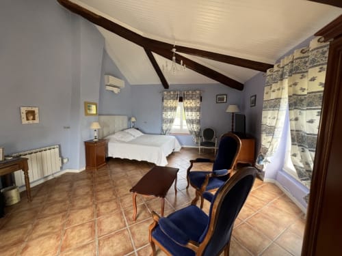 Chambre spacieuse à La Bastide des Princes à Caderousseavec murs lavande, poutres apparentes, carreaux en terre cuite et décor d'époque