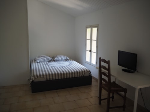 Chambre spacieuse de La Bastide des Princes avec literie rayée, TV, bureau et portes-fenêtres à Caderousse