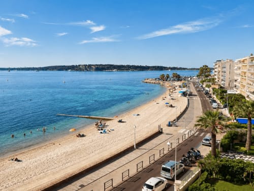 Sandy beach in Cannes with turquoise water, palm trees, waterfront promenade and Mediterranean sea views