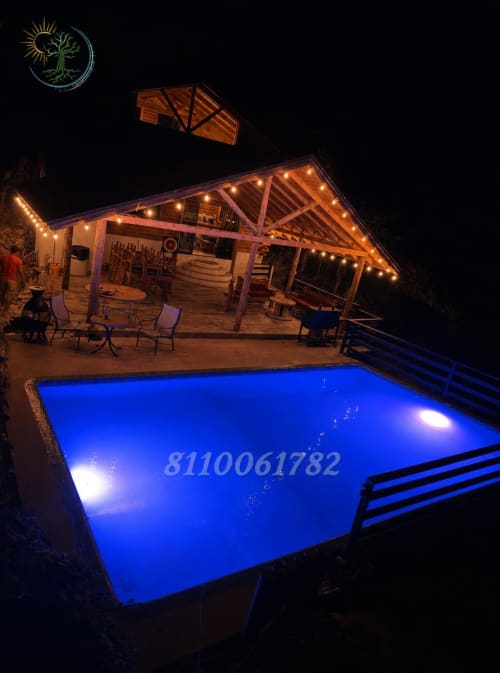 Piscina iluminada en azul durante la noche con casa de madera y luces cálidas en el hotel Tierra Cielo & SoLuna en Potrero de