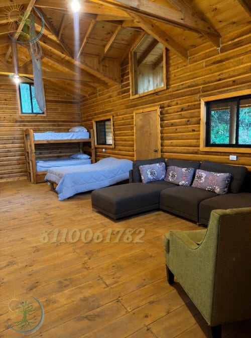 Amplia habitación de cabaña de madera en Tierra Cielo & SoLuna con literas, sofá negro y vistas a las montañas en Potrero de Serna