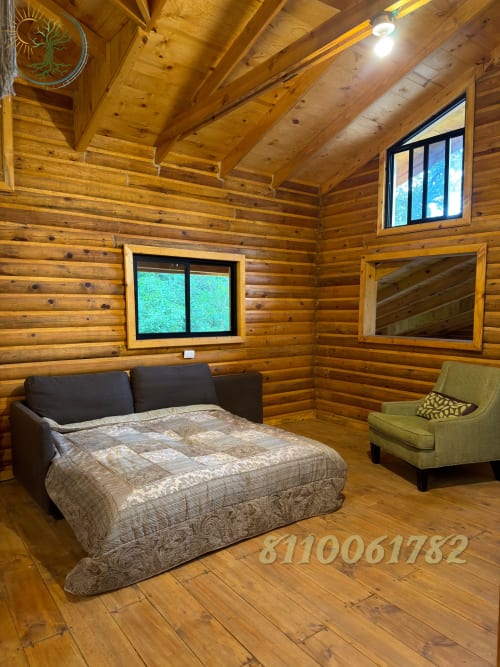 Dormitorio rústico de cabaña de troncos en Tierra Cielo & SoLuna con cama queen, sillón verde, vigas de madera y vistas a la montaña