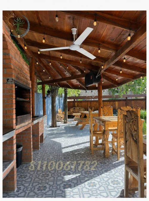 Patio rústico techado con vigas de madera, ventilador de techo, chimenea, muebles de comedor y planta decorativa en Tierra Cielo &