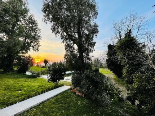 Sentiero nel giardino al tramonto del Ponteronico Resort a Sessa Aurunca, con alberi alti, erba rigogliosa e cielo dorato