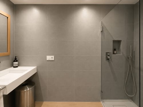 Baño moderno en apartamento Holibai Baiona con azulejos grises, lavabo blanco, ducha de lluvia y estanterías empotradas