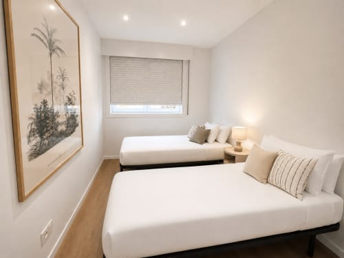 Moderno dormitorio doble en apartamento de Baiona con camas blancas, suelos de madera, arte botánico en paredes y vistas a la ciudad