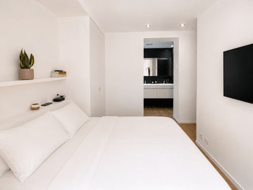 Dormitorio moderno en apartamento Campaiña, Baiona con cama blanca, baño privado, TV de pared y decoración minimalista