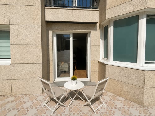 Terraza moderna de apartamento en Baiona con zona de descanso, mesa blanca y sillas que se abren al espacio interior