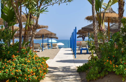 Pasillo de resort de playa con sombrillas y zonas de descanso en Grupo Inmohouse, Fuengirola, España