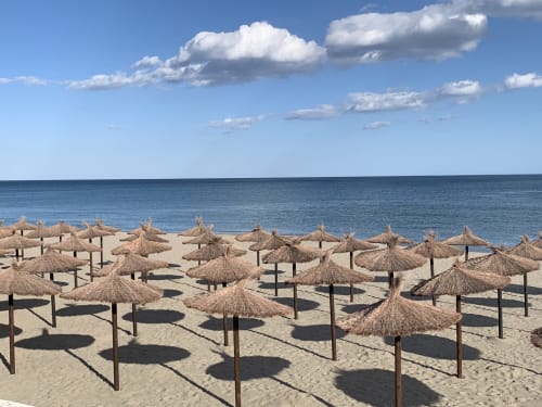 Vistas de playa con sombrillas de paja en arena blanca, mar y cielo azul cristalino en Fuengirola