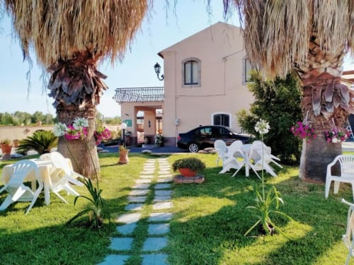 Cortile di Villa Laura B&B a Giardini Naxos con palme, sedie bianche e edificio rosa