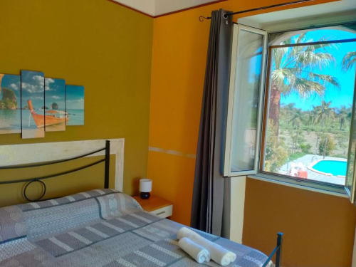 Camera luminosa di Villa Laura B&B a Giardini Naxos con muri arancioni, letto e vista terrazza su palme e piscina