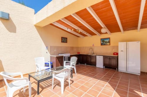 Sunny outdoor kitchen and dining area at Moraira Rental Villa with terracotta tiles, wooden beams, and white furniture