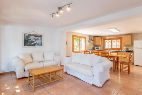 Bright living room in Moraira villa with cream sofas, wooden furniture, and open kitchen with wooden cabinets