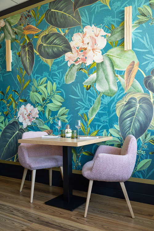 Intimate dining booth at Hôtel Restaurant Le S'Y with lavender chairs, wooden table, and vibrant tropical botanical wall