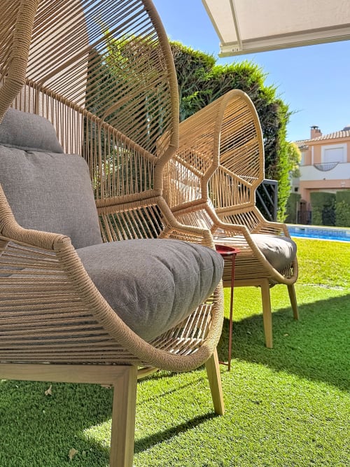 Chaises longues tissées modernes avec coussins gris sur pelouse verte à la location Estartit, piscine visible en arrière-plan