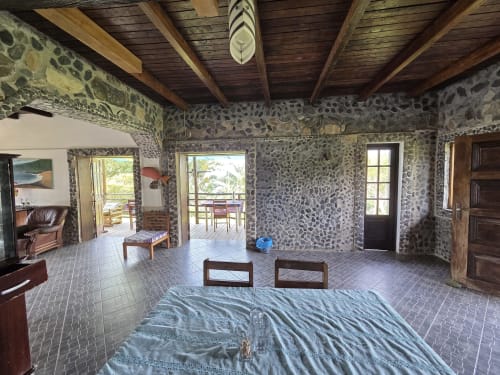 Quarto espaçoso com paredes de pedra, vigas de madeira e portas com vista para o mar na Equador Houses, São Tomé
