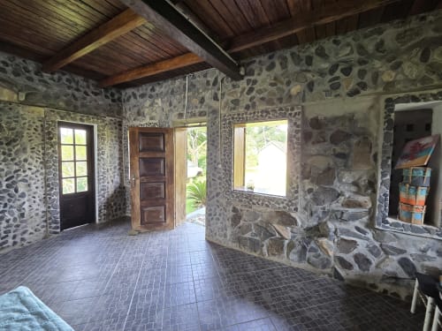 Amplo interior em pedra com vigas de madeira, piso de azulejos, portas e janelas de madeira na Equador Houses, São Tomé