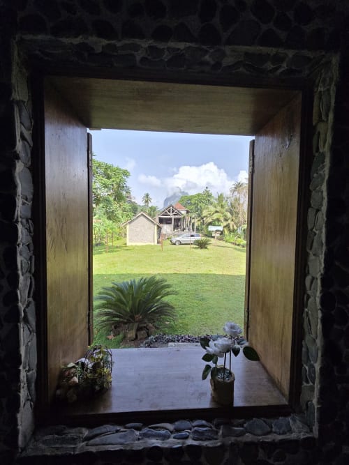 Portas de madeira abertas emolduradas pela vista do jardim tropical na Equador Houses, São Tomé, com gramado exuberante e montanhas ao fundo